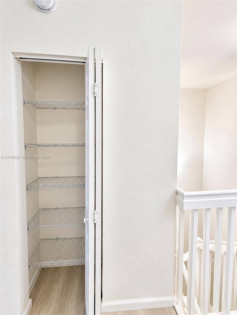 8800 NW 97th Avenue, #205, Doral, FL 33178 Storage closet featuring bi-fold doors, five tiers of wire shelving, and wood-finish flooring, accompanied by a white baluster railing