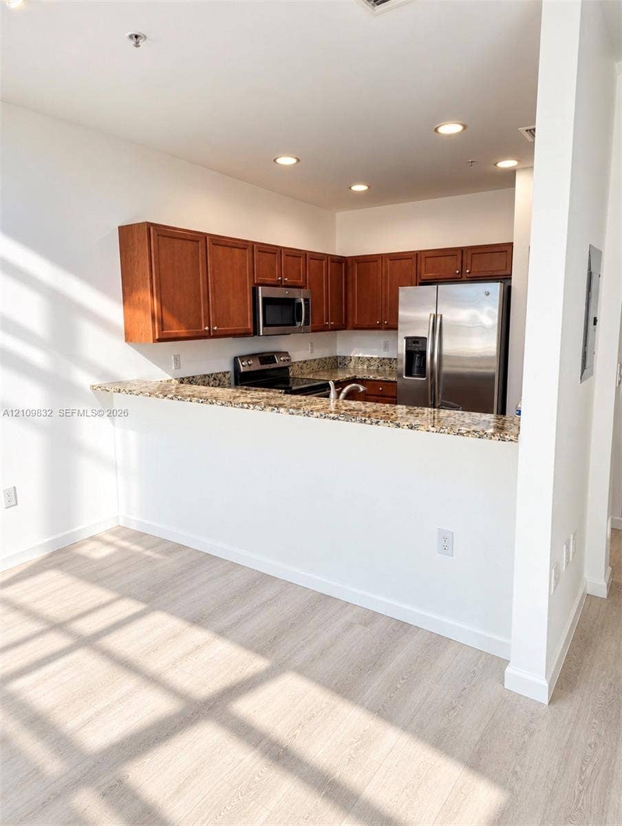 8800 NW 97th Avenue, #205, Doral, FL 33178 Kitchen featuring a peninsula with a stone countertop, wood-finish cabinetry, stainless steel appliances, and recessed lighting