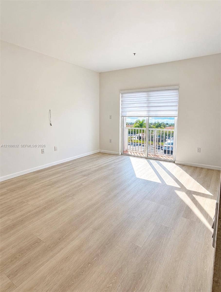 8800 NW 97th Avenue, #205, Doral, FL 33178 Light-filled room featuring wood-finish flooring, neutral wall paint, and sliding glass doors with an integrated shade opening to an exterior balcony