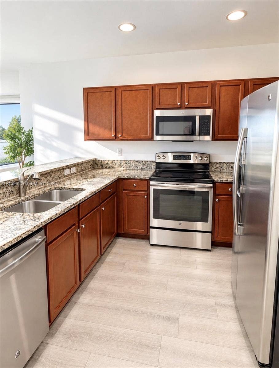 8800 NW 97th Avenue, #205, Doral, FL 33178 Kitchen featuring wood cabinetry, stone-finish countertops, stainless steel appliances, a double-basin undermount sink, and wood-finish flooring
