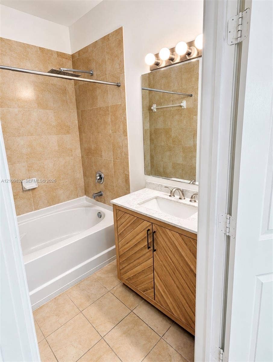 8800 NW 97th Avenue, #205, Doral, FL 33178 Bathroom featuring a wood-finish vanity with a stone countertop, an integrated under-mount sink, a tile-surround soaking tub, and wall-mounted light fixtures