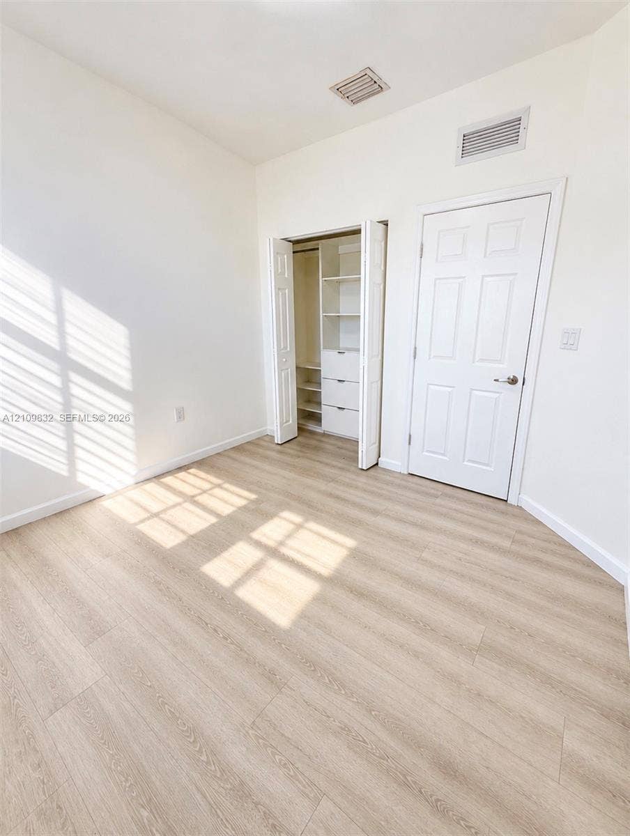 8800 NW 97th Avenue, #205, Doral, FL 33178 Room featuring wood-finish flooring, a six-panel interior door, and a built-in closet with integrated shelving and drawer storage