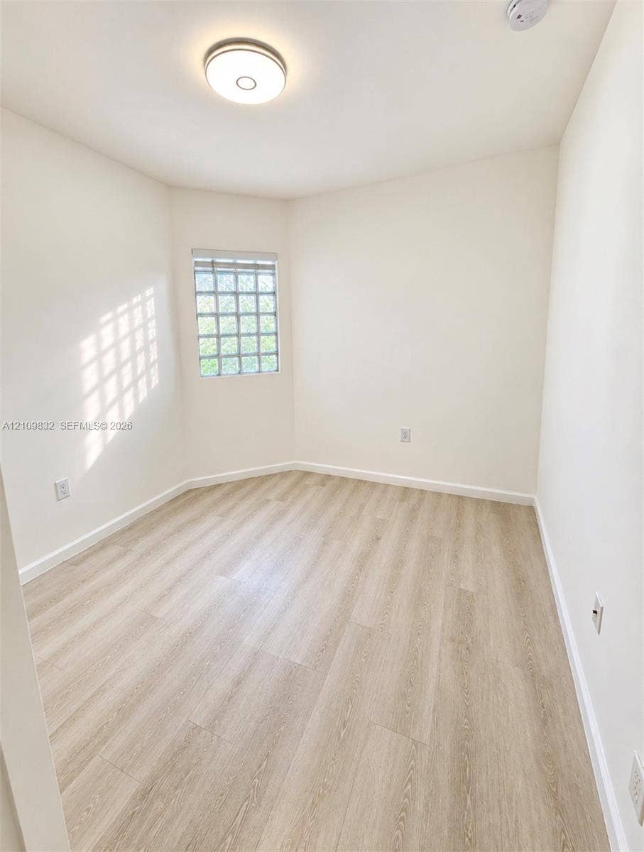 8800 NW 97th Avenue, #205, Doral, FL 33178 Neutral-toned room featuring wood-finish flooring, glass block window, and circular flush-mount ceiling lighting