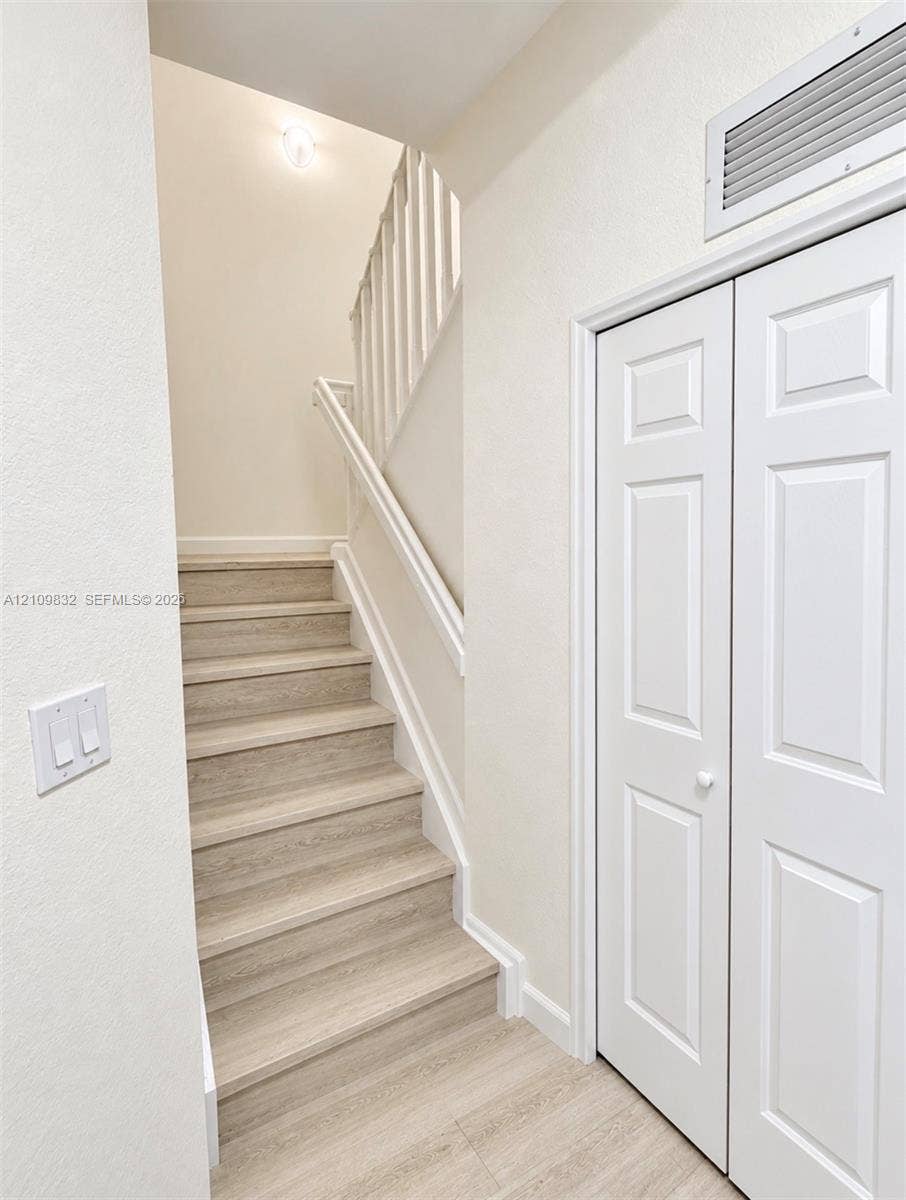 8800 NW 97th Avenue, #205, Doral, FL 33178 Staircase featuring wood-finish treads and a white wooden balustrade, paired with a white paneled bifold closet door
