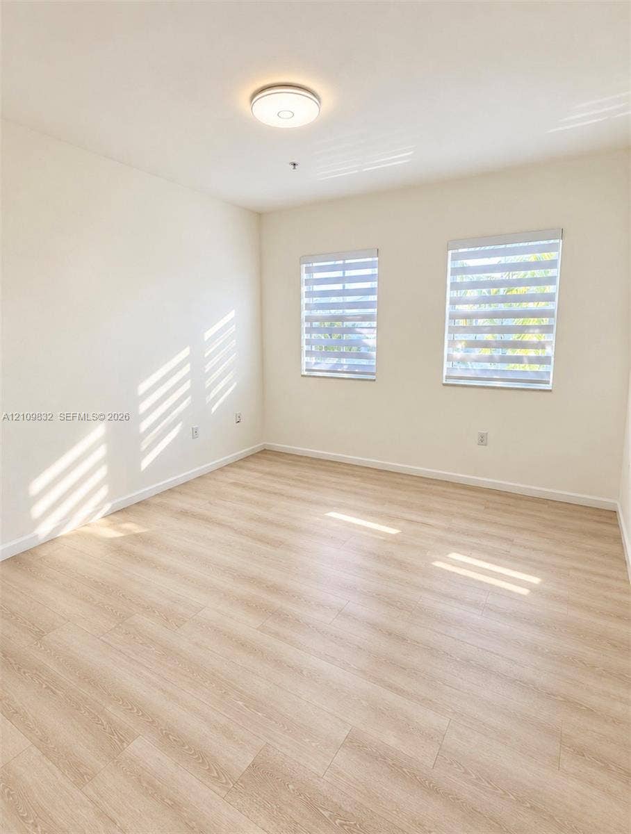 8800 NW 97th Avenue, #205, Doral, FL 33178 Neutral-toned interior space featuring wood-finish flooring, dual windows with installed roller shades, and a flush-mount ceiling light fixture