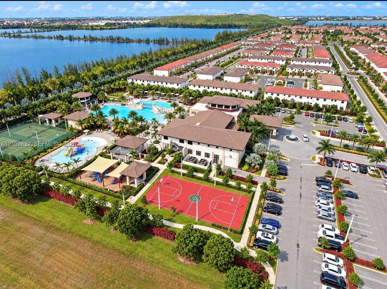 8800 NW 97th Avenue, #205, Doral, FL 33178 Aerial perspective featuring a swimming pool, multiple tennis courts, a basketball court, a splash pad, and waterfront grounds