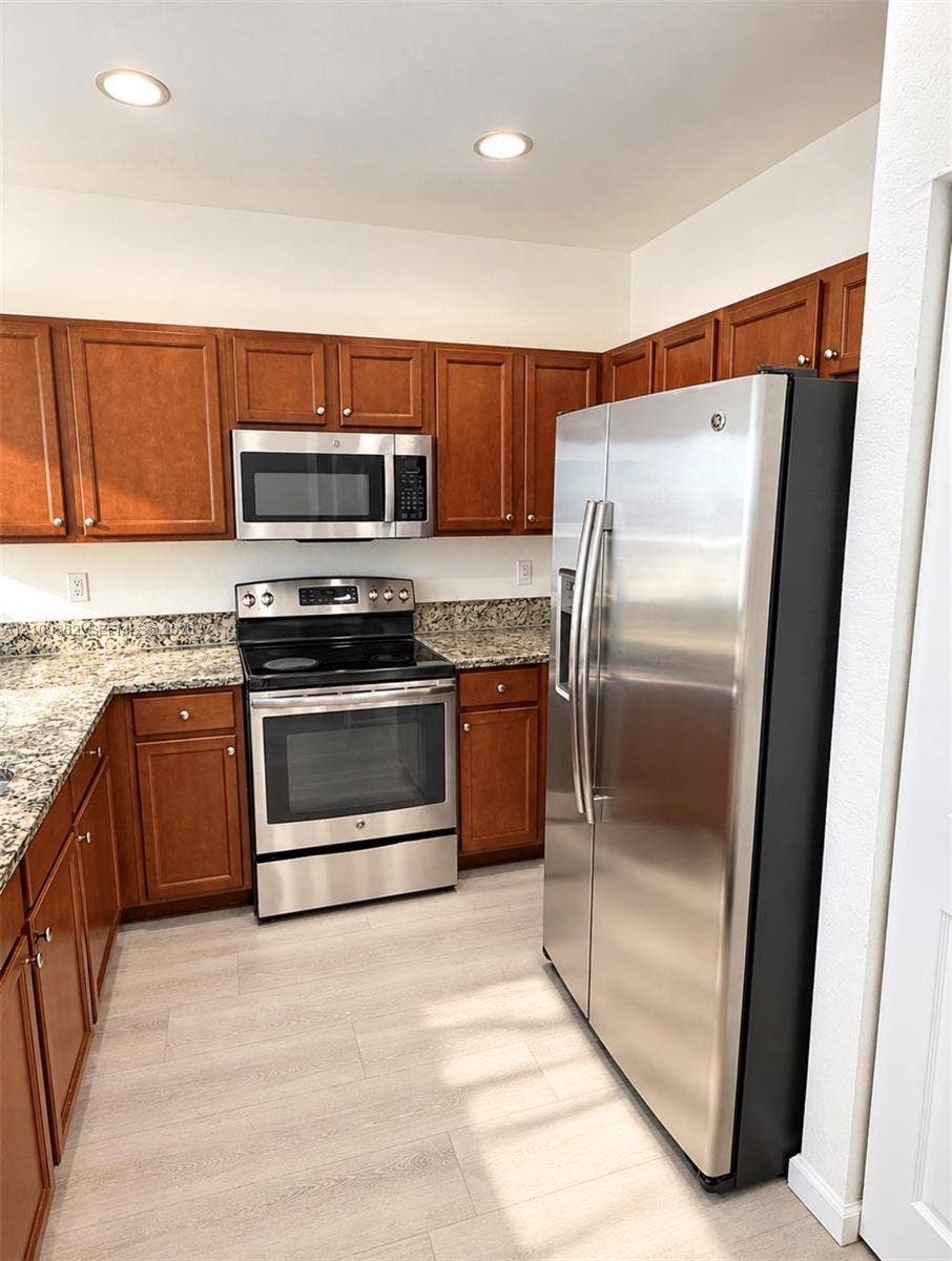 8800 NW 97th Avenue, #205, Doral, FL 33178 Kitchen featuring stained wood cabinetry, stone-finish countertops, stainless steel appliances, and light-toned wood-finish flooring
