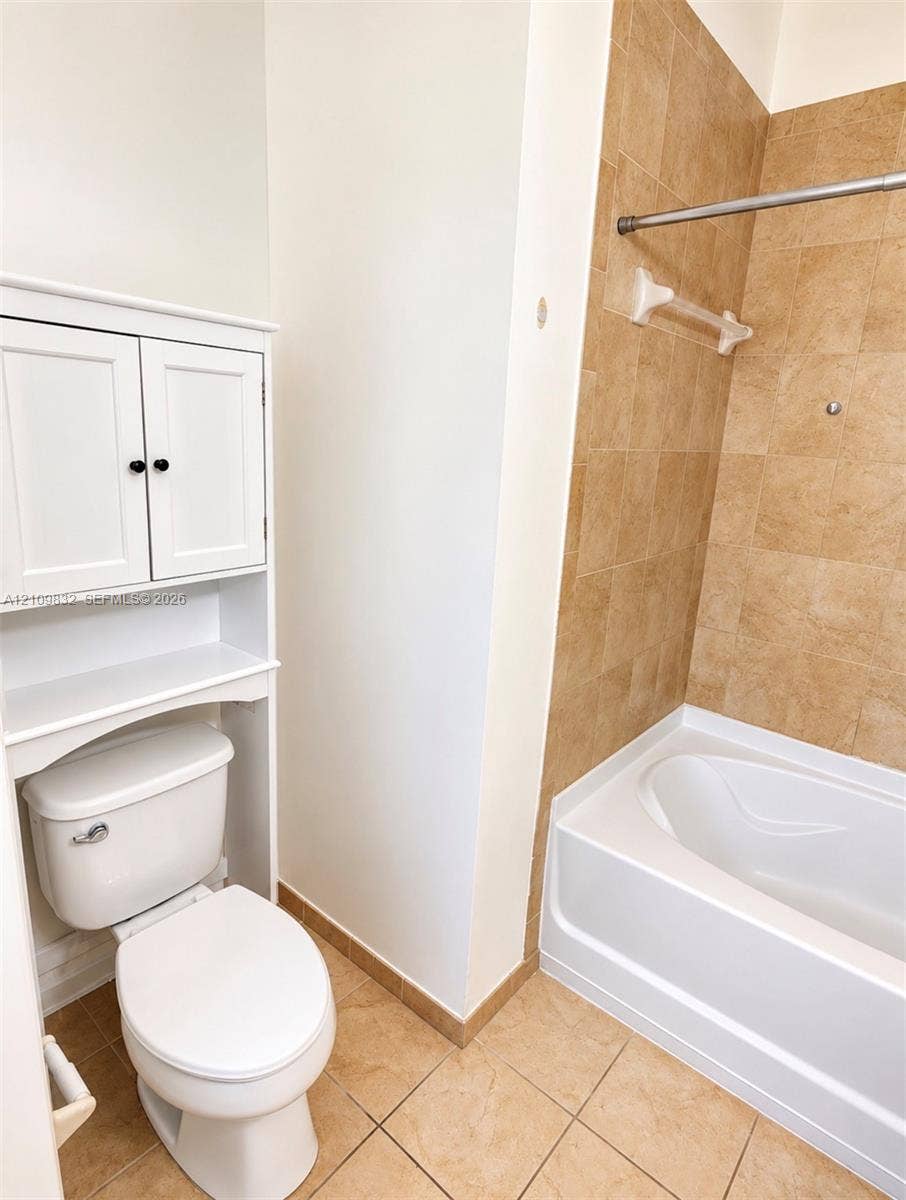 8800 NW 97th Avenue, #205, Doral, FL 33178 Bathroom featuring a white built-in storage cabinet, porcelain toilet, soaking tub, neutral-tone tile surround, and tile flooring
