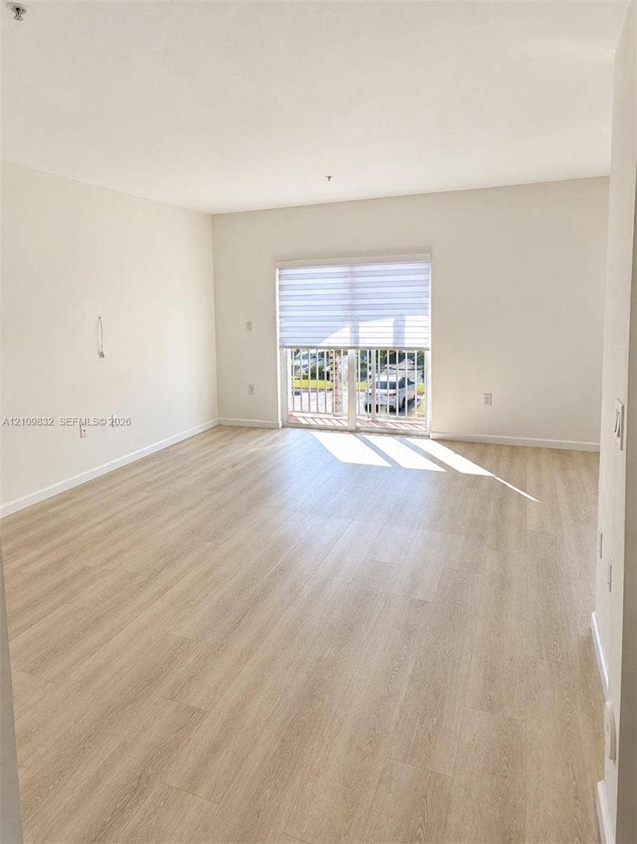 8800 NW 97th Avenue, #205, Doral, FL 33178 Open-concept living space featuring wood-finish flooring, neutral wall paint, and a sliding glass door providing access to a private balcony