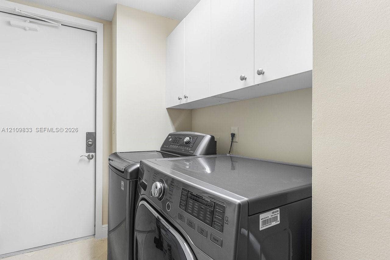 530 Ocean Drive, #405, Juno Beach, FL 33408 Laundry area featuring white built-in upper cabinetry with polished metal hardware and a solid-core entry door with a deadbolt lock