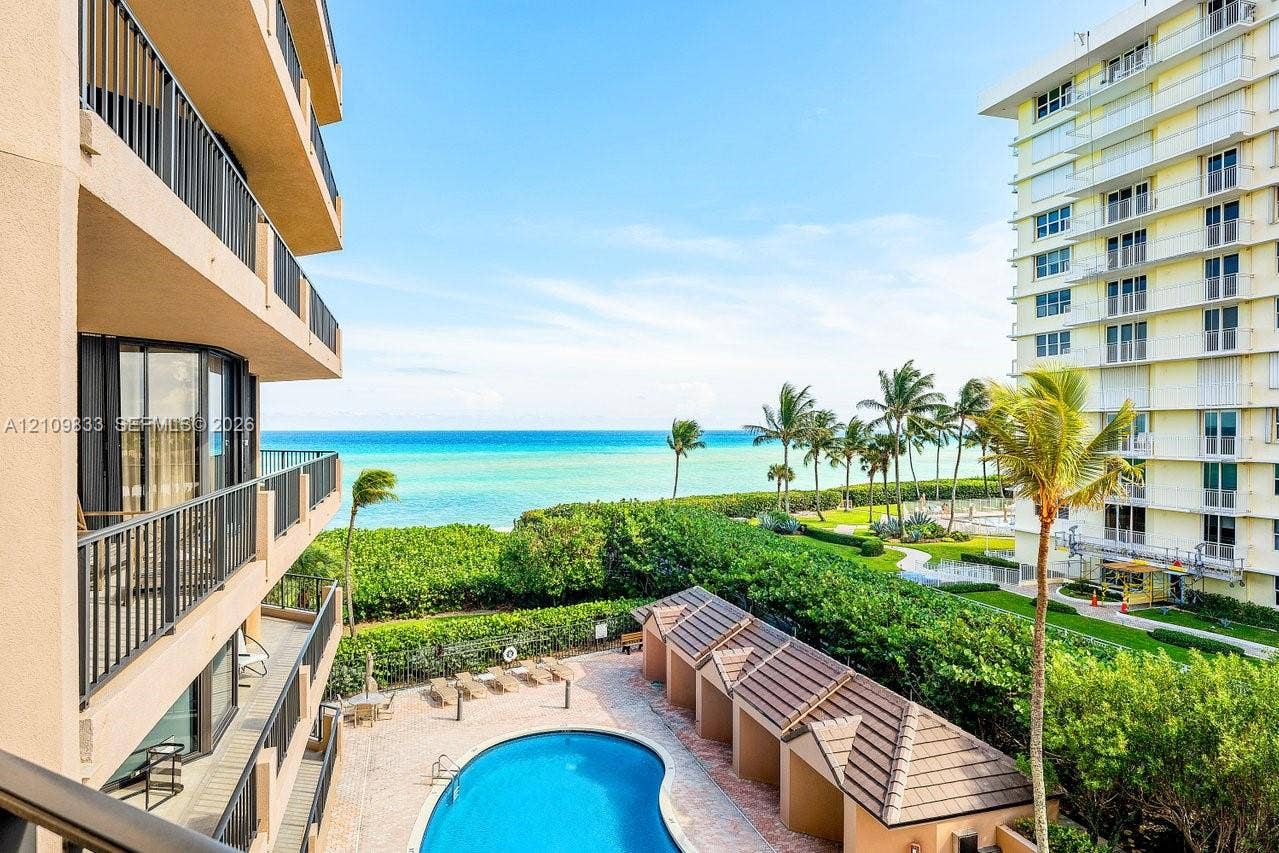 530 Ocean Drive, #405, Juno Beach, FL 33408 Private balcony with black metal railings overlooking a community swimming pool, poolside cabanas, landscaped grounds, and the ocean
