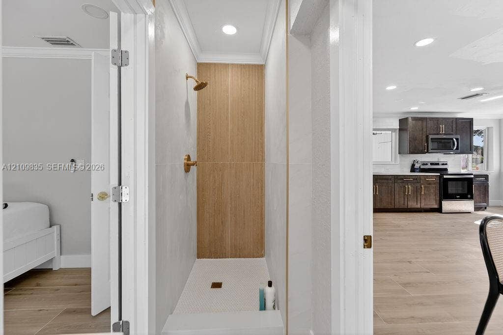 756 Cinnamon Road, North Palm Beach, North Palm Beach, FL 33408 Walk-in shower featuring gold-toned fixtures, a wood-finish tile accent wall, white wall tiling, and recessed lighting
