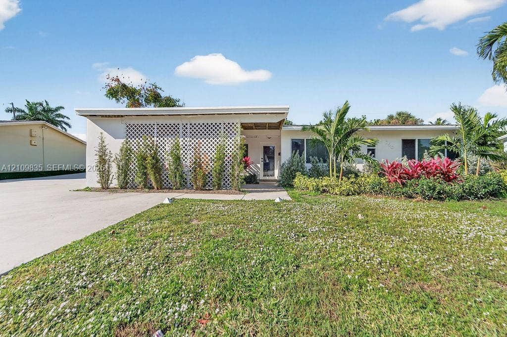 756 Cinnamon Road, North Palm Beach, North Palm Beach, FL 33408 Single-story exterior featuring a flat roofline, decorative lattice screen, concrete driveway, and established tropical landscaping