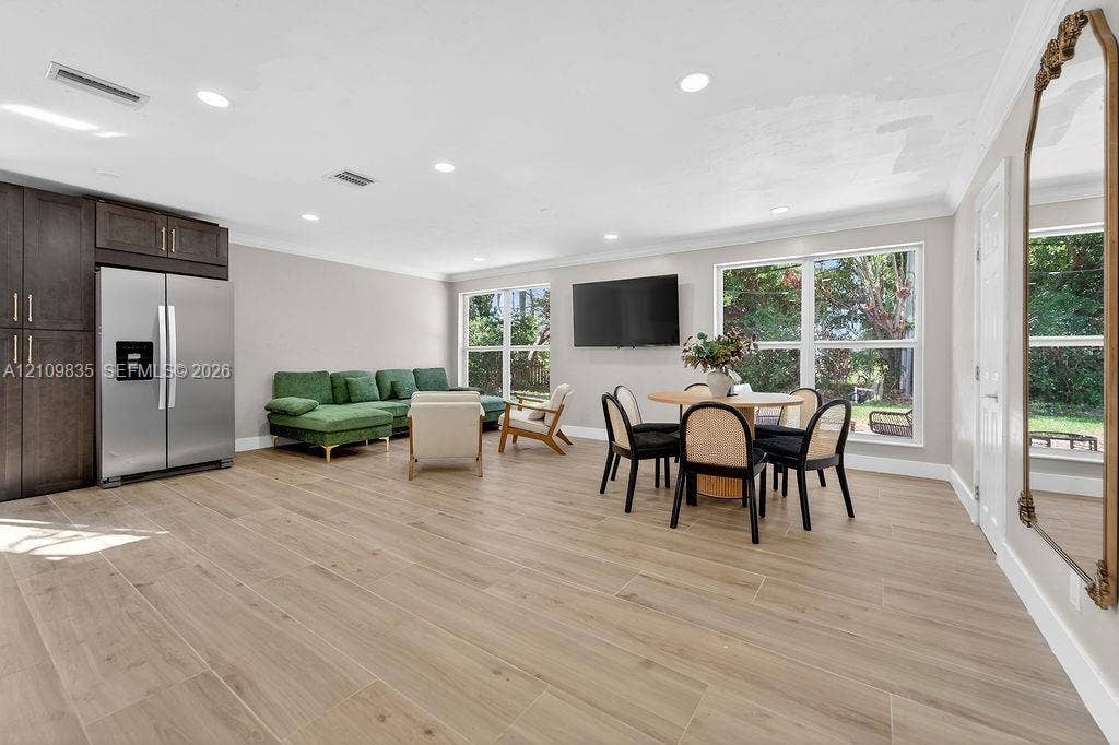 756 Cinnamon Road, North Palm Beach, North Palm Beach, FL 33408 Open-concept space featuring wood-finish flooring, recessed lighting, crown molding, large windows, and built-in dark wood cabinetry with a stainless steel refrigerator