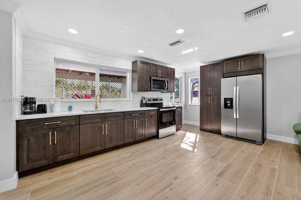 756 Cinnamon Road, North Palm Beach, North Palm Beach, FL 33408 Kitchen featuring dark wood-finish cabinetry, white solid-surface countertops, wood-finish flooring, stainless steel appliances, and a white tile backsplash