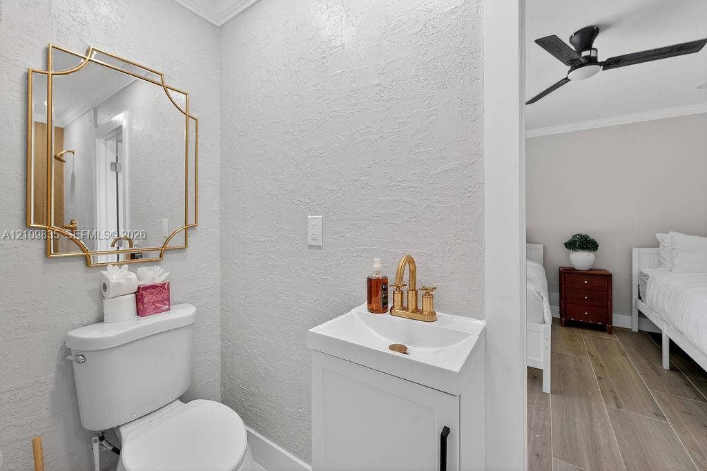 756 Cinnamon Road, North Palm Beach, North Palm Beach, FL 33408 Bathroom featuring a geometric gold-framed mirror, white pedestal vanity with metallic gold hardware, bridge-style faucet, and wood-finish flooring