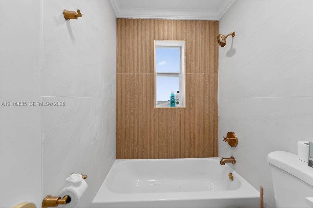 756 Cinnamon Road, North Palm Beach, North Palm Beach, FL 33408 Bathtub enclosure featuring white wall tiling, a vertical wood-finish accent tile surround, and metallic-finish plumbing fixtures
