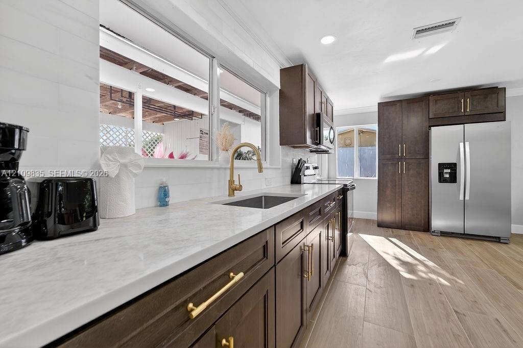 756 Cinnamon Road, North Palm Beach, North Palm Beach, FL 33408 Kitchen featuring dark-finish cabinetry, stone-style countertops, wood-finish flooring, a stainless steel refrigerator, and a gold-tone faucet with an undermount sink