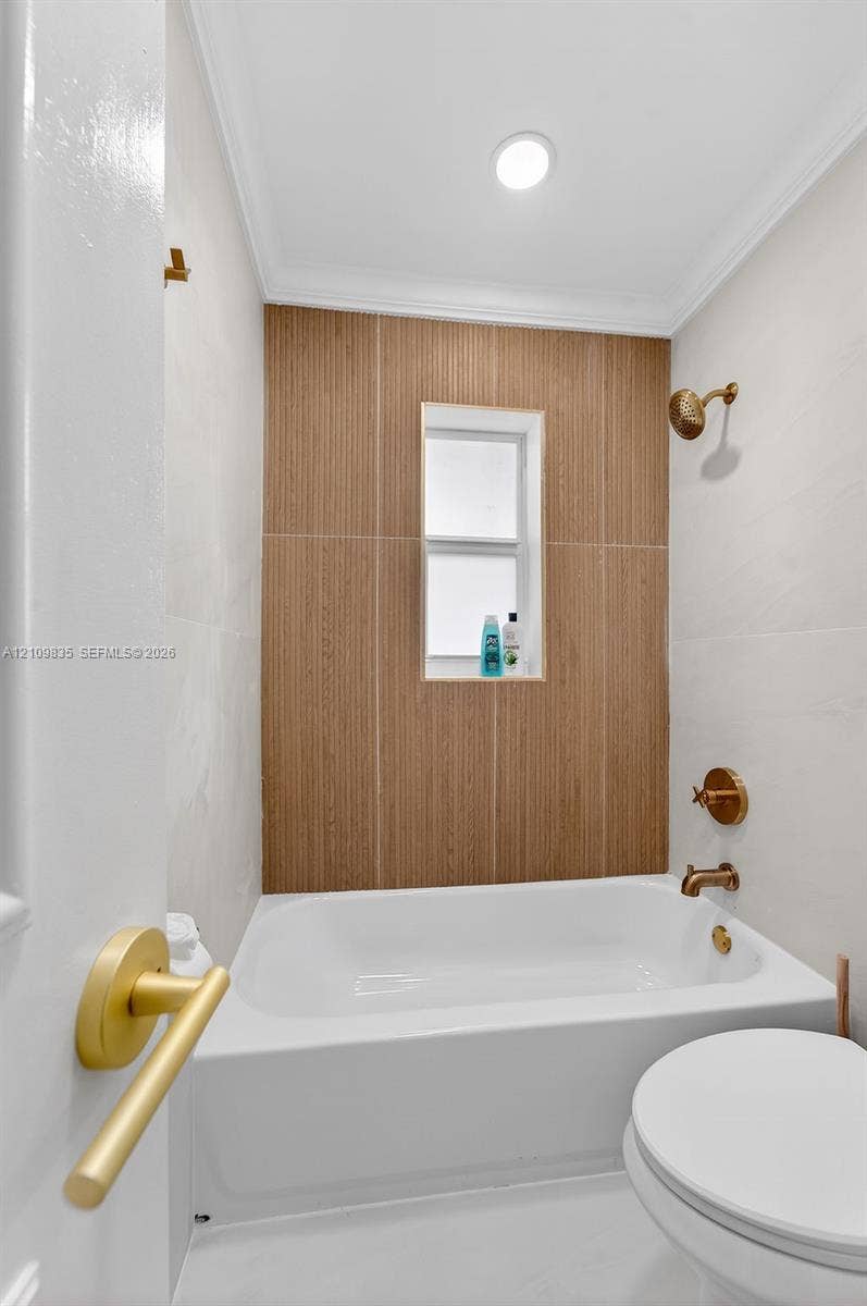 756 Cinnamon Road, North Palm Beach, North Palm Beach, FL 33408 Bathroom featuring a deep soaking tub, wood-finish tile surround, recessed window niche, and brass-tone fixtures