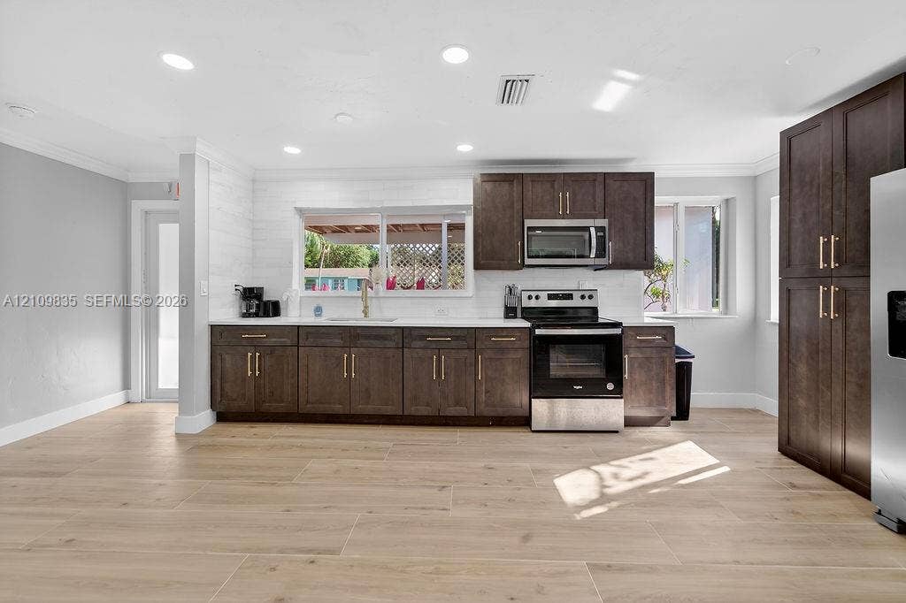 756 Cinnamon Road, North Palm Beach, North Palm Beach, FL 33408 Kitchen featuring dark-toned cabinetry with gold-finish hardware, stainless steel appliances, white subway-style backsplash, light-toned wood-finish flooring, and recessed ceiling lighting
