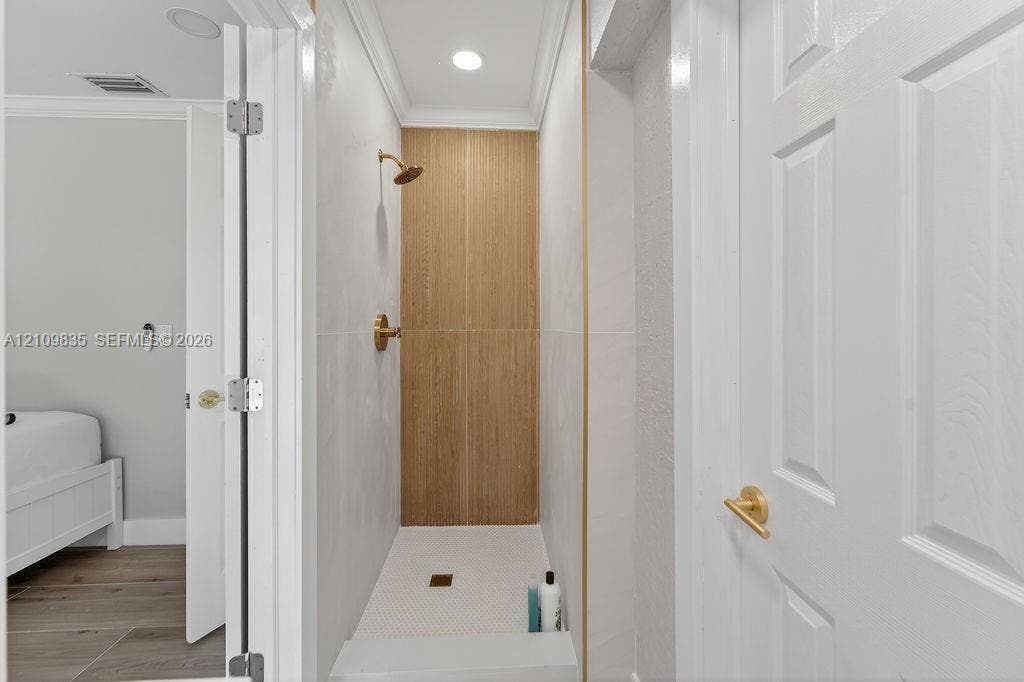 756 Cinnamon Road, North Palm Beach, North Palm Beach, FL 33408 Shower stall featuring light-toned tile walls, vertical wood-finish tile accent, brushed gold shower fixture, and a mosaic tile floor