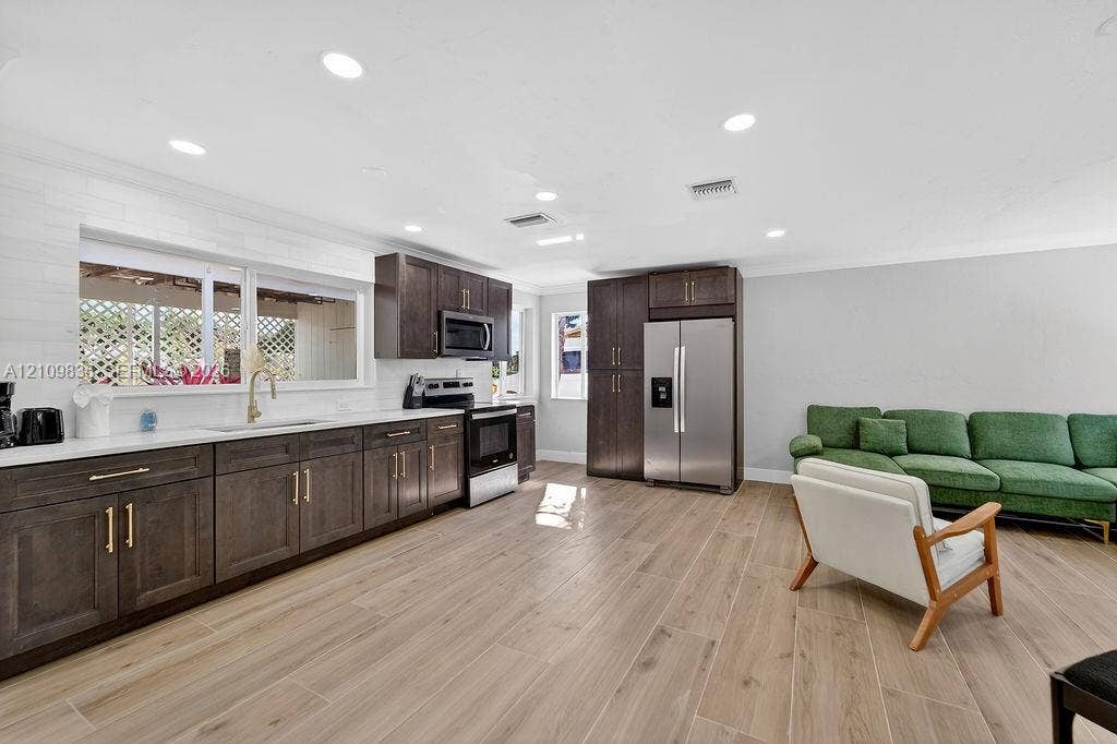 756 Cinnamon Road, North Palm Beach, North Palm Beach, FL 33408 Kitchen featuring dark wood-finish cabinetry, brass-toned hardware, white countertops, stainless steel appliances, and wood-finish tile flooring
