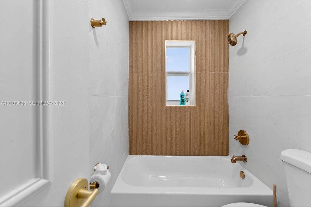 756 Cinnamon Road, North Palm Beach, North Palm Beach, FL 33408 Bathroom featuring white wall tile, a wood-finish tile shower surround, brass-tone fixtures, a built-in tub, and an inset window