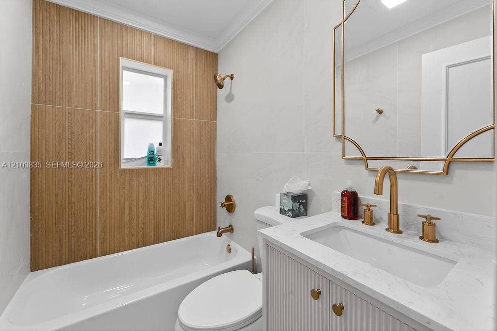 756 Cinnamon Road, North Palm Beach, North Palm Beach, FL 33408 Bathroom featuring a wood-finish tile tub surround, white vanity with stone-style countertop, metallic gold-tone hardware, and decorative wall-mounted mirror