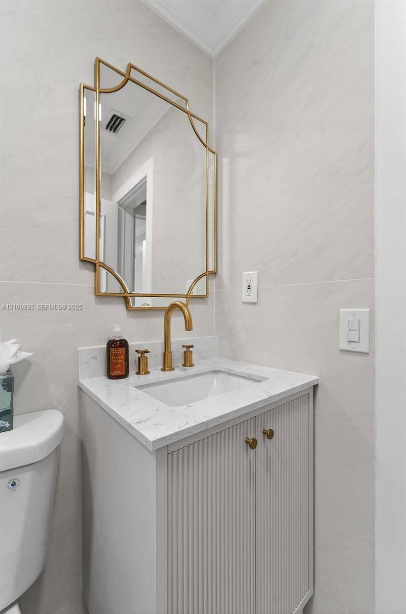 756 Cinnamon Road, North Palm Beach, North Palm Beach, FL 33408 Bathroom vanity featuring a fluted cabinet base, stone-composite countertop, brushed gold faucet, and matching geometric wall-mounted mirror