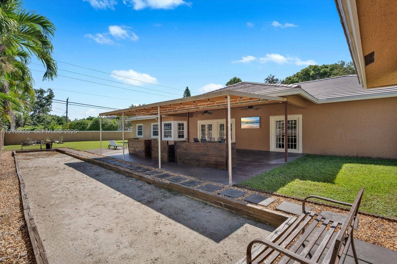 7901 SW 97th Street, Miami, FL 33156 Covered extended patio featuring a concrete slab foundation, recessed ceiling fans, and a complemented by an outdoor bocce ball court and a manicured lawn *