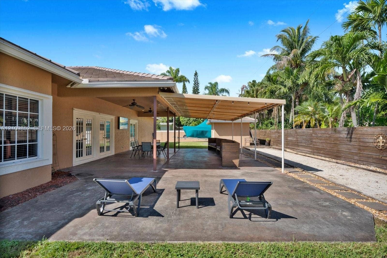 7901 SW 97th Street, Miami, FL 33156 Expansive concrete patio featuring a covered outdoor living area, ceiling fans, and wood-paneled privacy fencing in the back and a concrete wall with lighting on the sides of the house and in the front *