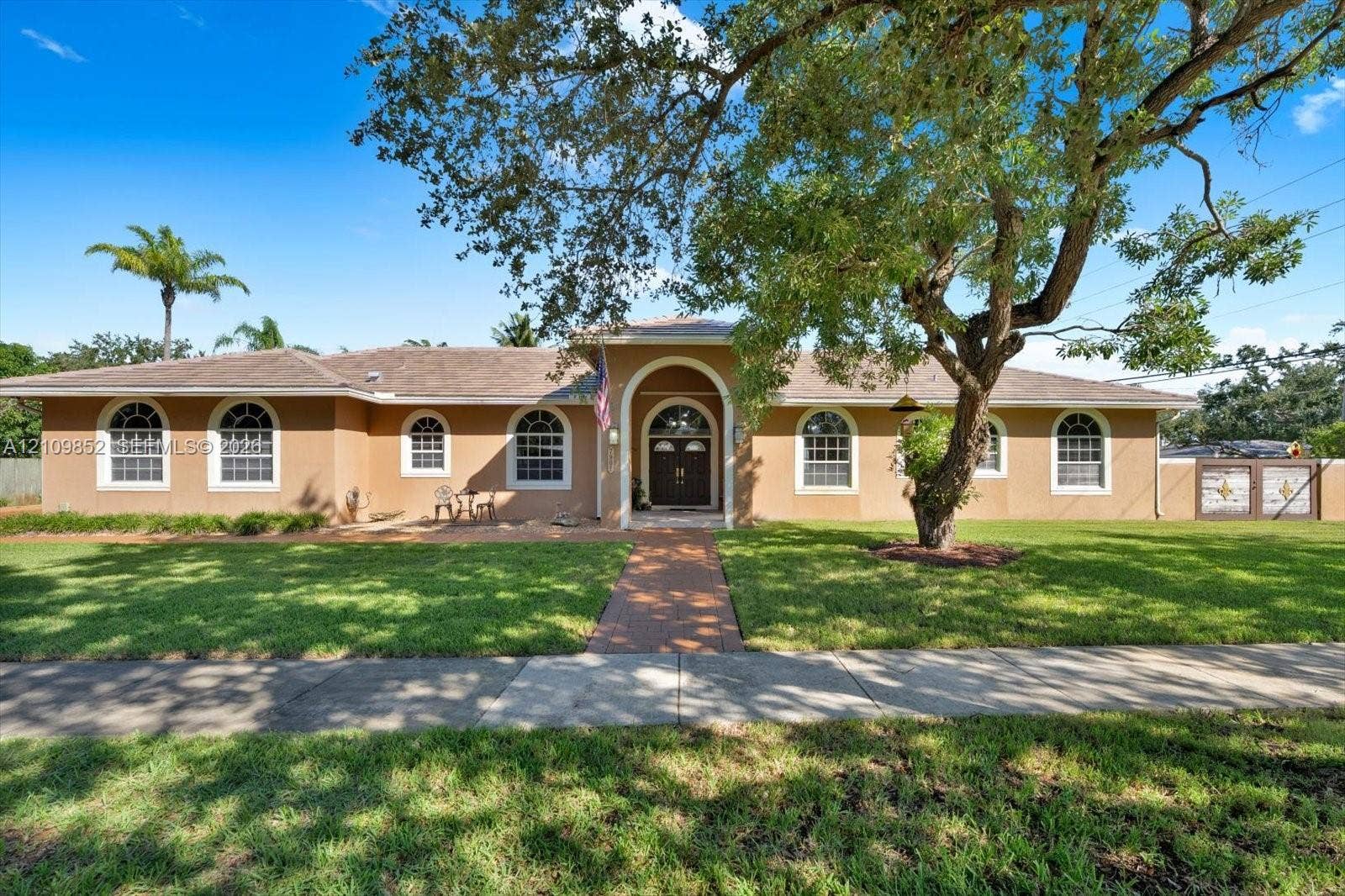 7901 SW 97th Street, Miami, FL 33156 Single-story exterior featuring a stamped concrete walkway, arched entryway, and multiple arched windows * concrete wall in the front with custom metal gates *