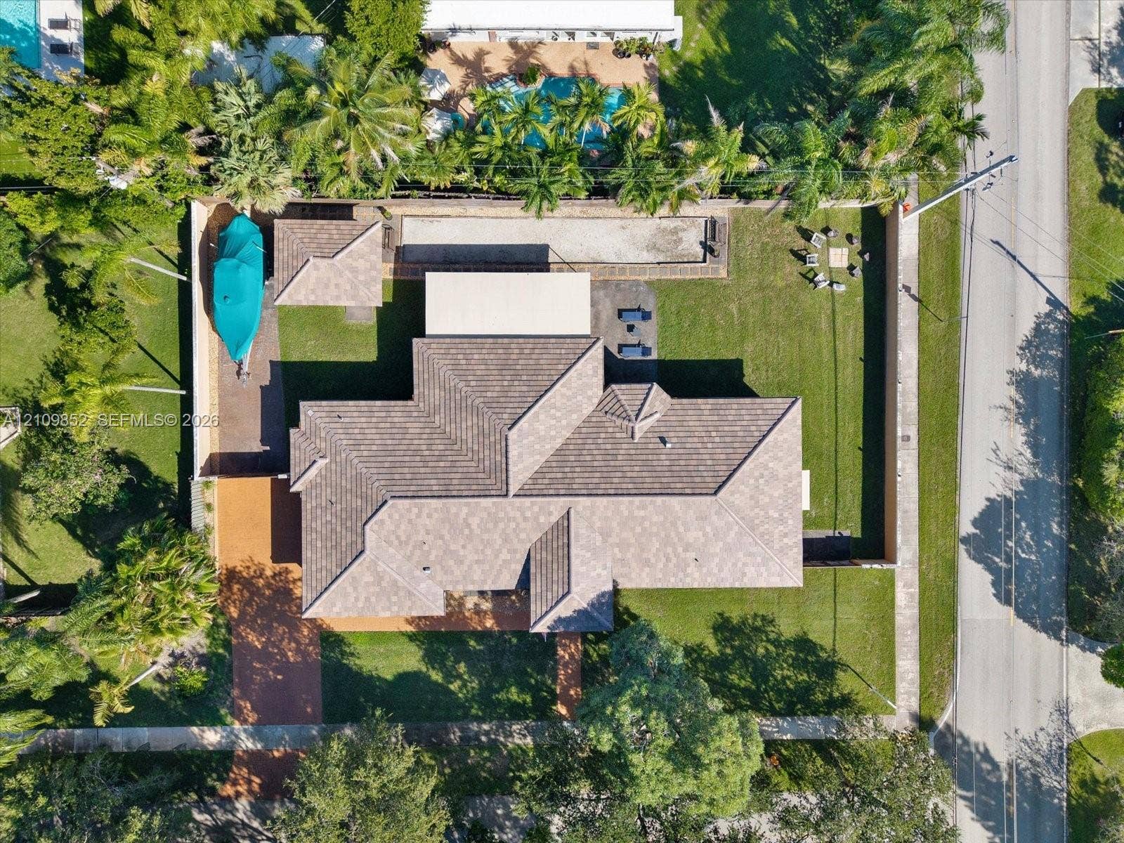 7901 SW 97th Street, Miami, FL 33156 Aerial perspective featuring a multi-hipped roofline, expansive grass lawn, paved driveway, enclosed perimeter wall, and mature landscaping