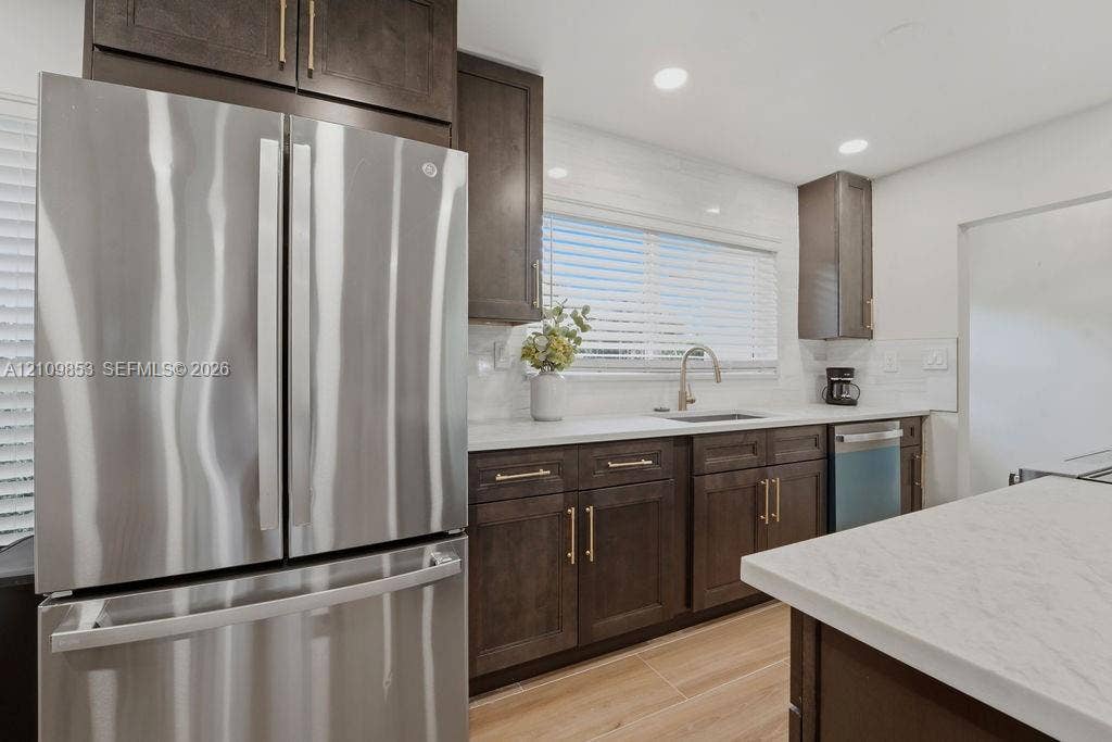 800 Alamanda Drive, North Palm Beach, North Palm Beach, FL 33408 Kitchen featuring dark-finish cabinetry, stainless steel appliances, light-toned stone-finish countertops, subway tile backsplash, and wood-finish flooring