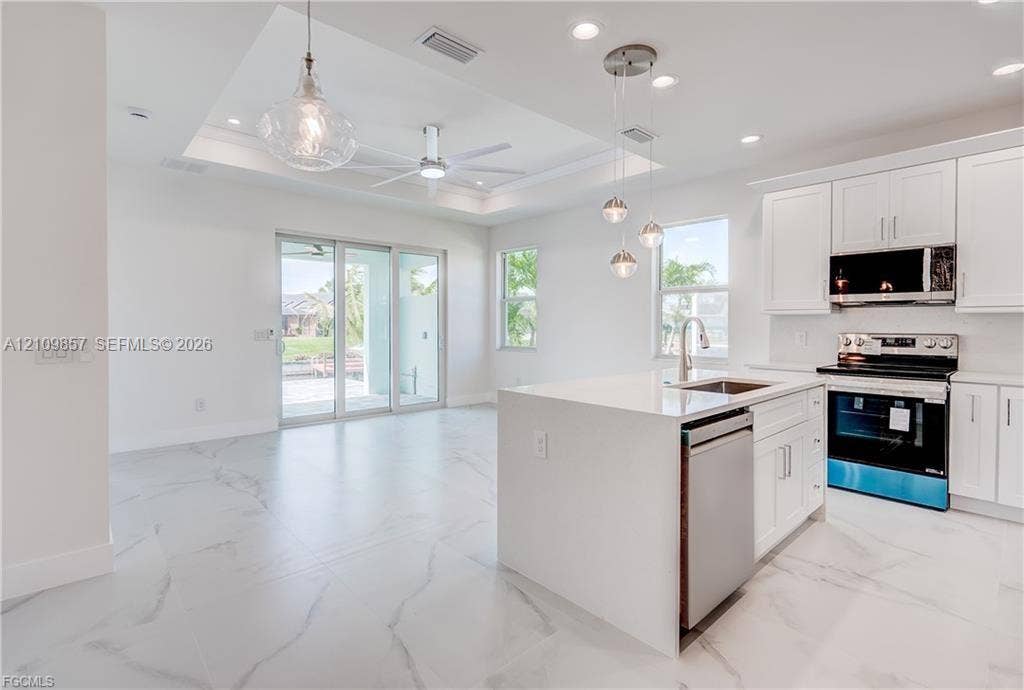 1105 SE 38th Street, Cape Coral, FL 33904 Kitchen featuring white cabinetry, a center island with a stone-finish countertop, stainless steel appliances, and large-format tile flooring with a marble pattern, capped with a tray ceiling and recessed lighting