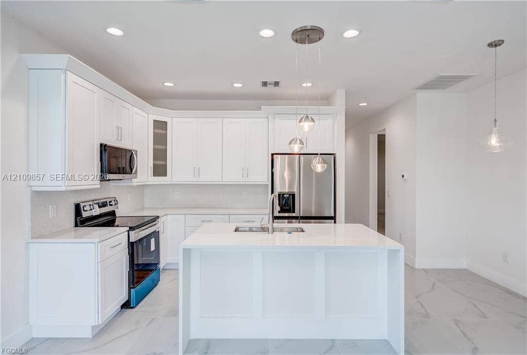 1105 SE 38th Street, Cape Coral, FL 33904 Kitchen featuring white shaker-style cabinetry, a central island with a solid-surface countertop, stainless steel appliances, and tile flooring