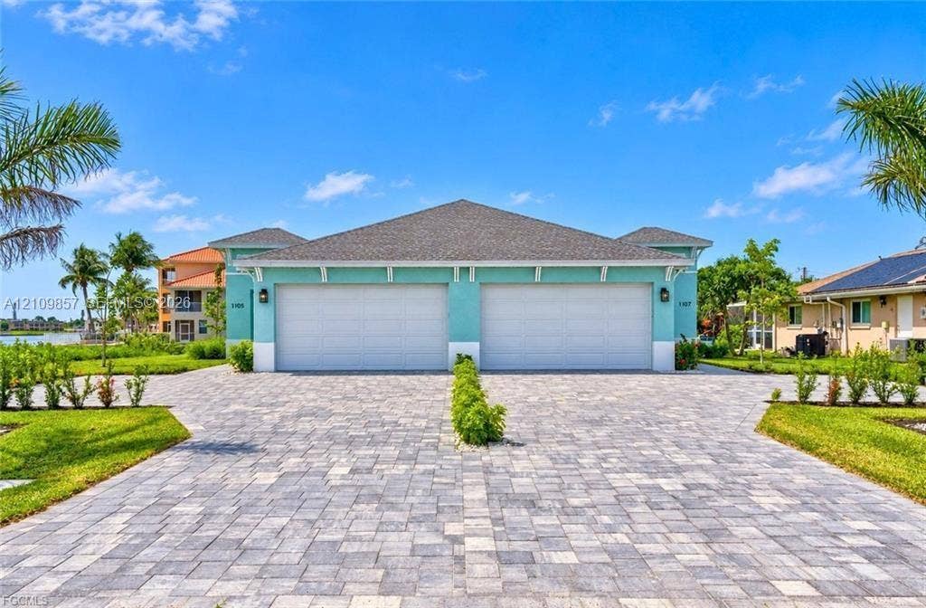 1105 SE 38th Street, Cape Coral, FL 33904 Exterior facade featuring dual garage doors, a stone-paver driveway, and professional landscaping