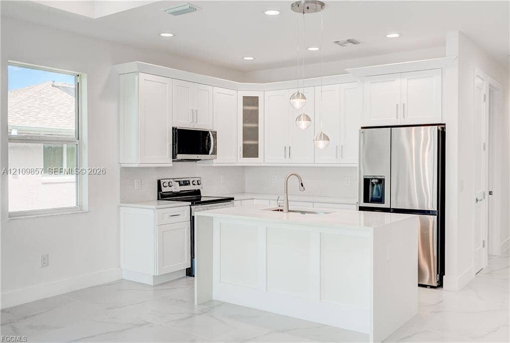 1105 SE 38th Street, Cape Coral, FL 33904 Kitchen featuring white shaker-style cabinetry, a central island with a waterfall edge, stone countertops, stainless steel appliances, and pendant lighting