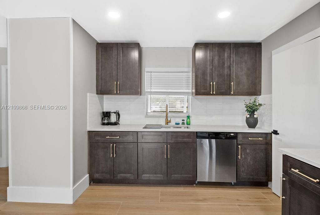 736 Prosperity Farms Road, North Palm Beach, North Palm Beach, FL 33408 Kitchen featuring dark-finish cabinetry, gold-tone hardware, white stone-surface countertops, subway tile backsplash, and stainless steel dishwasher