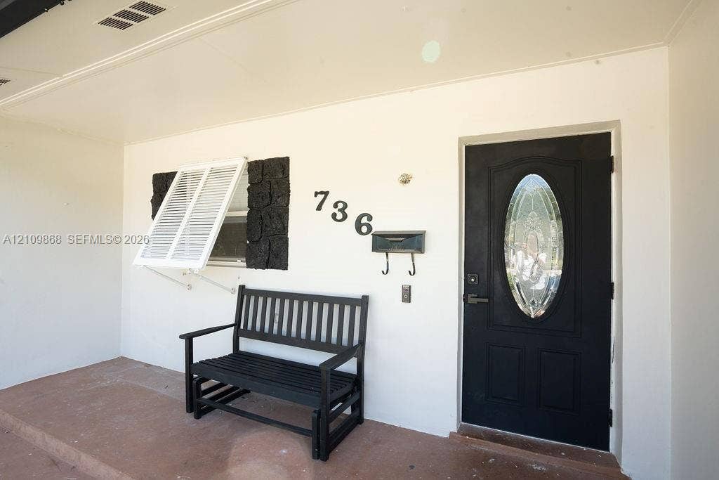 736 Prosperity Farms Road, North Palm Beach, North Palm Beach, FL 33408 Covered entryway featuring a black front door with an oval glass insert, stone accent wall details, white exterior shutters, and a concrete porch