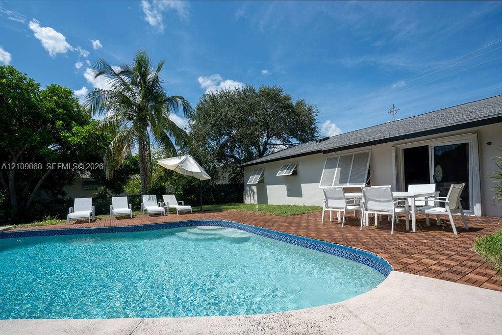 736 Prosperity Farms Road, North Palm Beach, North Palm Beach, FL 33408 In-ground swimming pool featuring a curved design and integrated stairs, complemented by a patio area with interlocking wood-finish tiles and exterior shutters