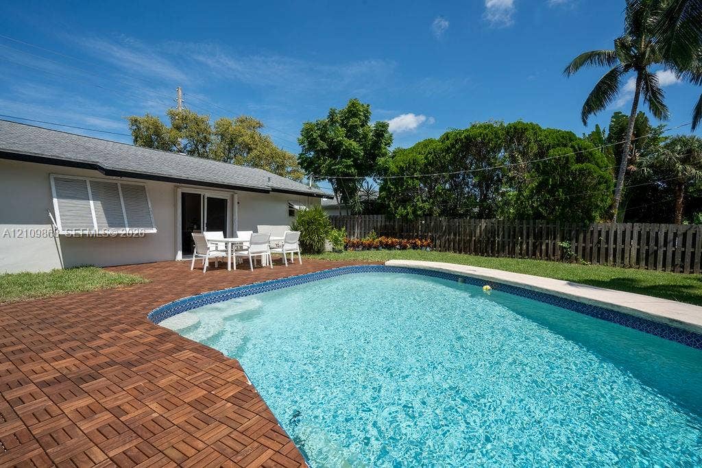 736 Prosperity Farms Road, North Palm Beach, North Palm Beach, FL 33408 In-ground pool with stone-tiled edging, custom wood-tile patio decking, wood-plank perimeter fencing, and mature landscaping