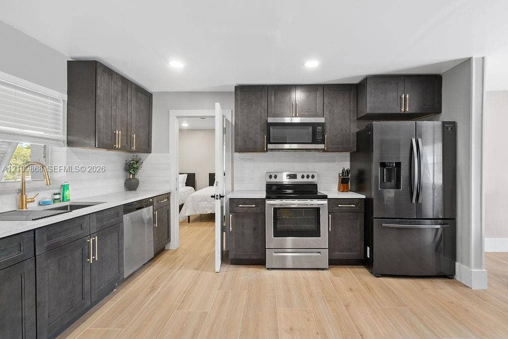 736 Prosperity Farms Road, North Palm Beach, North Palm Beach, FL 33408 Kitchen featuring dark-stained cabinetry, wood-finish flooring, quartz countertops, stainless steel appliances, and a gold-tone faucet