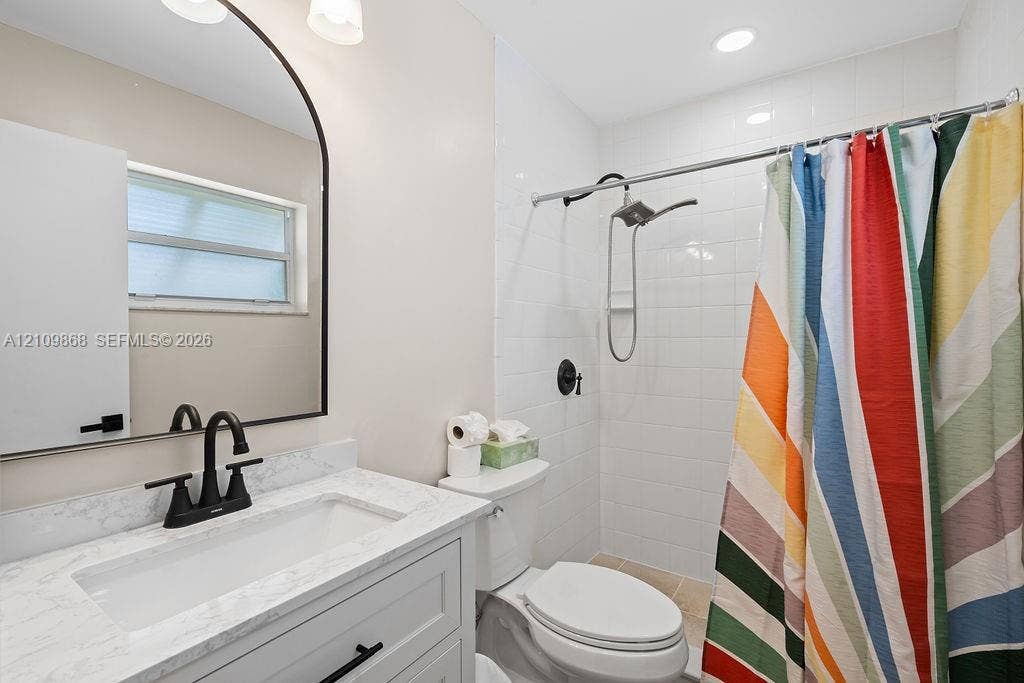 736 Prosperity Farms Road, North Palm Beach, North Palm Beach, FL 33408 Bathroom featuring a stone-look countertop vanity with a matte black faucet, a rounded arch mirror, and a tub-shower combination with white subway tile surround and matte black fixtures