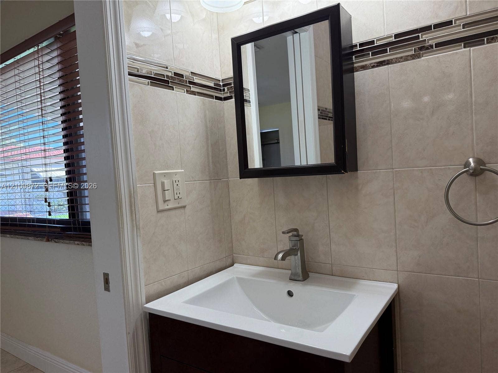 811 NE 10th Street, #5, Hallandale Beach, Hallandale Beach, FL 33009 Dark wood-finish vanity with a white rectangular basin, metallic single-handle faucet, integrated medicine cabinet, and ceramic wall tiling with decorative glass tile inlay