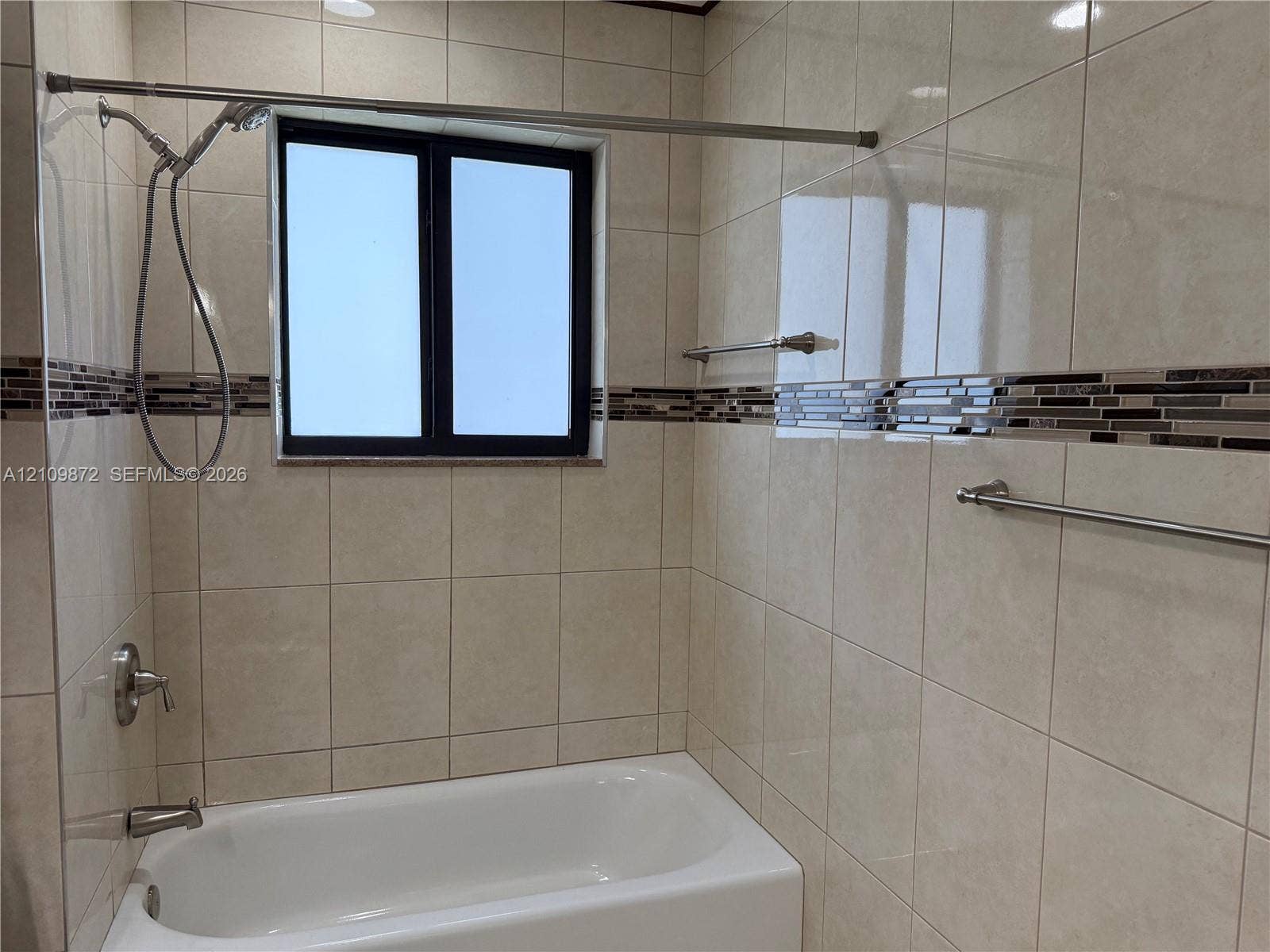 811 NE 10th Street, #5, Hallandale Beach, Hallandale Beach, FL 33009 Full-height tile shower surround featuring a decorative mosaic tile accent border, inset window, brushed nickel plumbing fixtures, and integrated towel bars