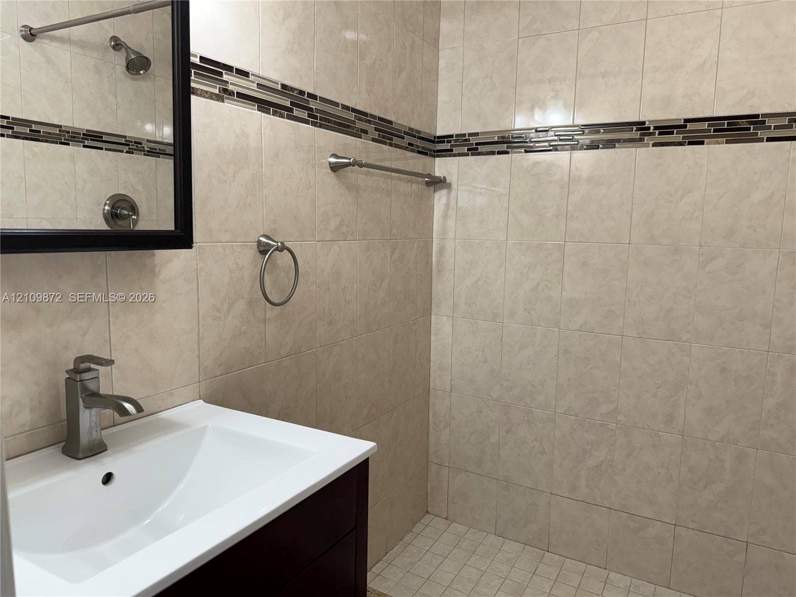811 NE 10th Street, #5, Hallandale Beach, Hallandale Beach, FL 33009 Bathroom featuring a dark wood vanity with a white integrated sink, polished metal faucet, walk-in tiled shower with a decorative mosaic tile inlay, and brushed nickel hardware