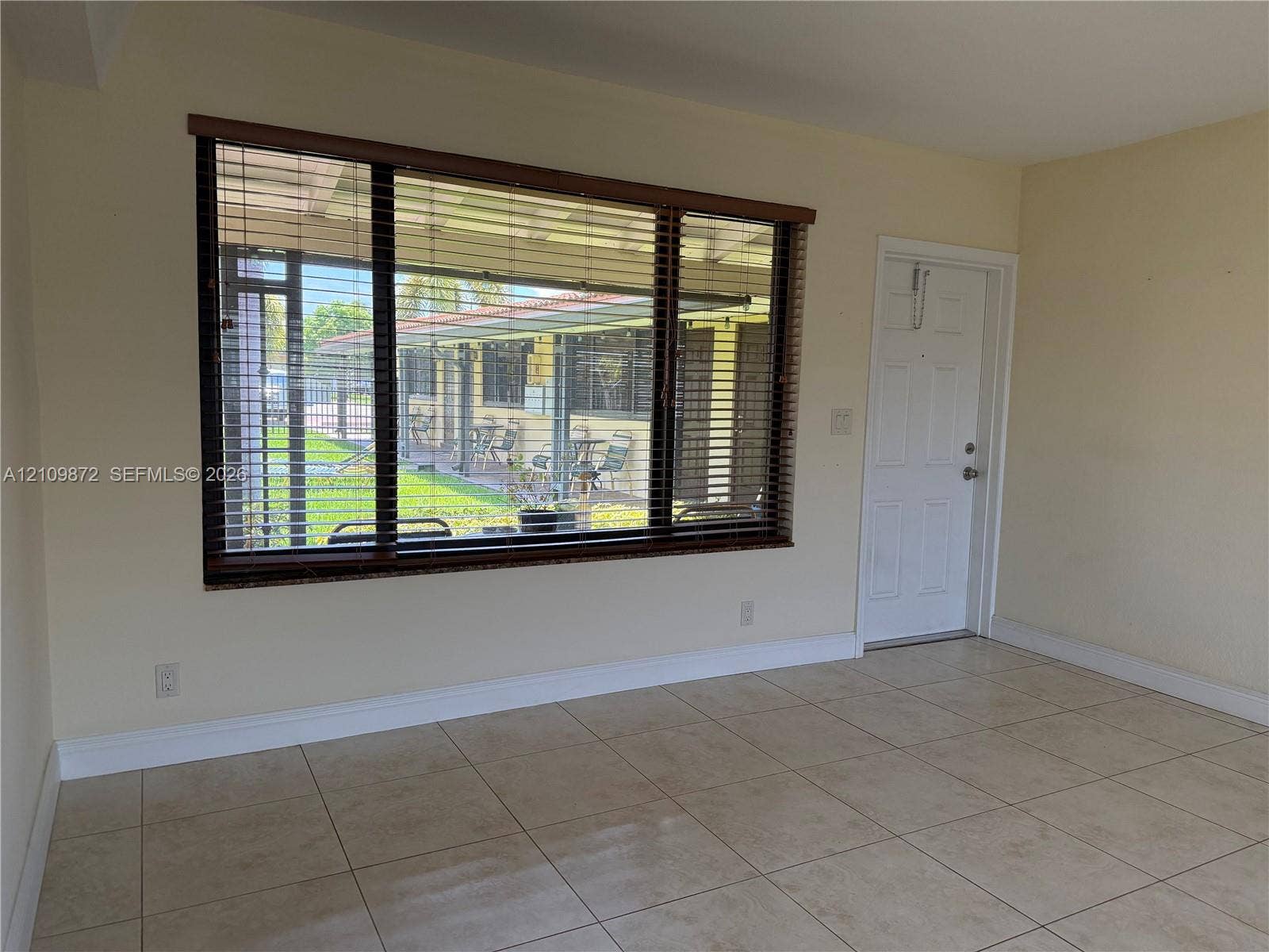 811 NE 10th Street, #5, Hallandale Beach, Hallandale Beach, FL 33009 Neutral-toned interior space featuring large-format ceramic tile flooring, a expansive picture window with wood-finish horizontal blinds, and a paneled entry door