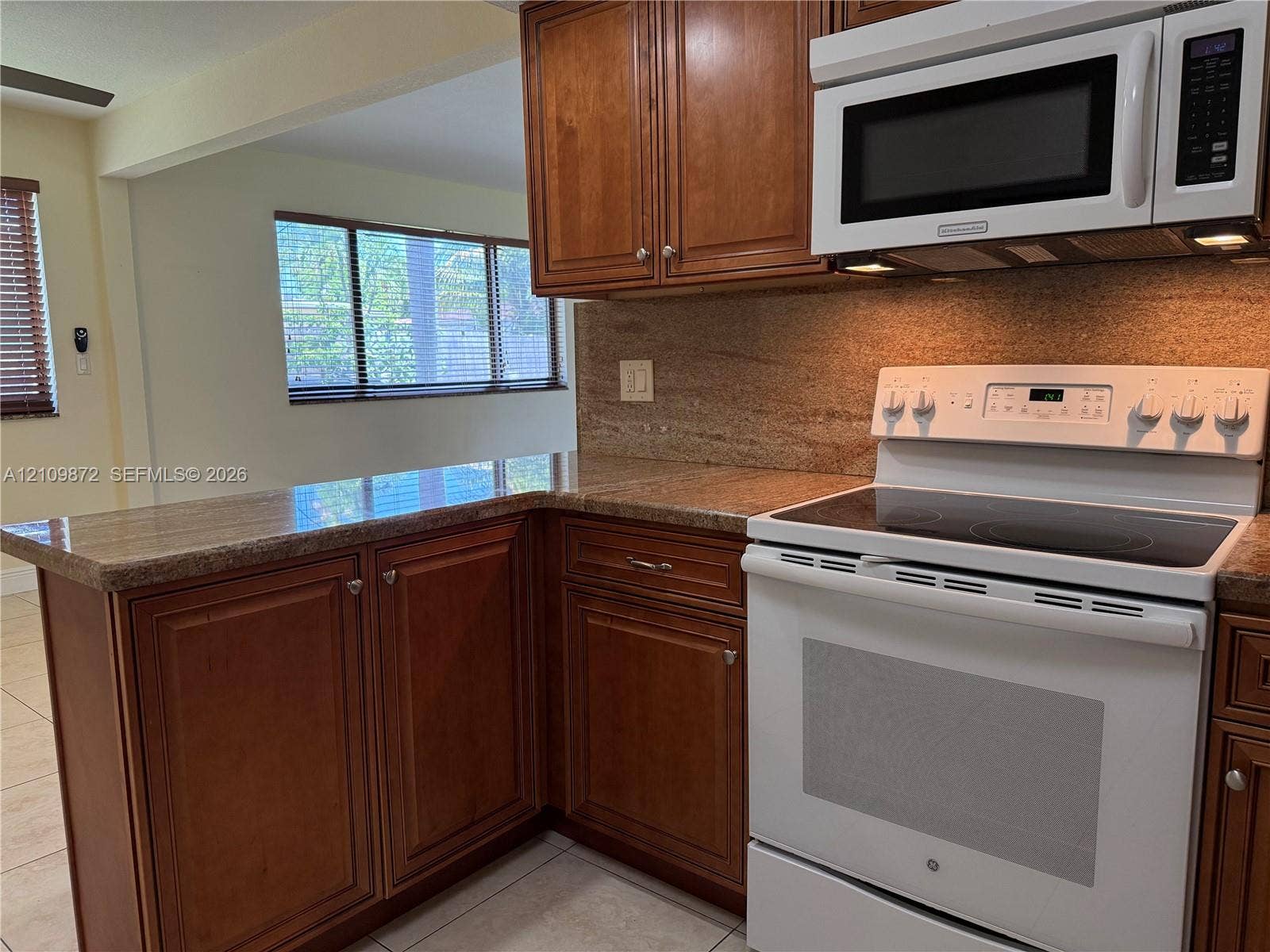 811 NE 10th Street, #5, Hallandale Beach, Hallandale Beach, FL 33009 Kitchen featuring stained wood cabinetry, stone-surface countertops, stone-tile backsplash, and white appliances including an electric range and built-in microwave