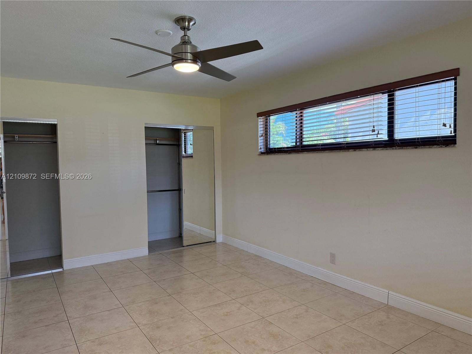811 NE 10th Street, #5, Hallandale Beach, Hallandale Beach, FL 33009 Neutral-toned tile flooring, brushed-metal ceiling fan with integrated light fixture, horizontal window with slat blinds, and dual closets with sliding mirrored doors